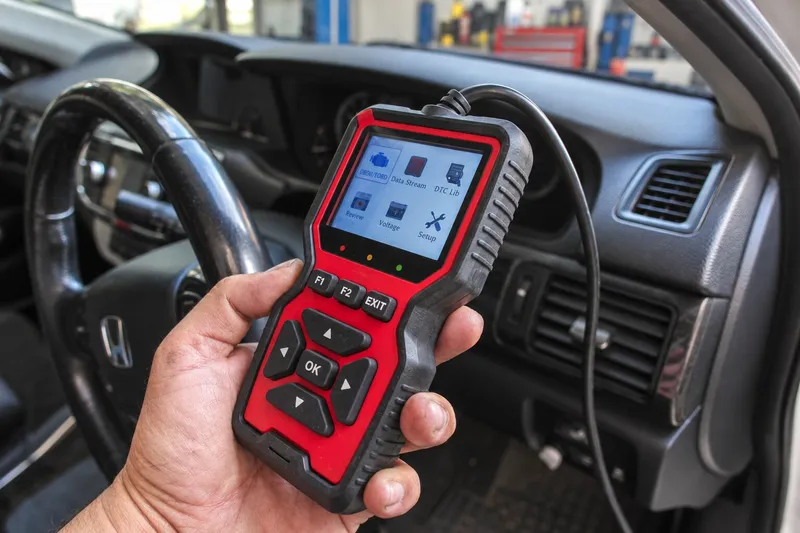 Tester OBD2 portabil ținut în habitaclu, cu cablul de conectare vizibil